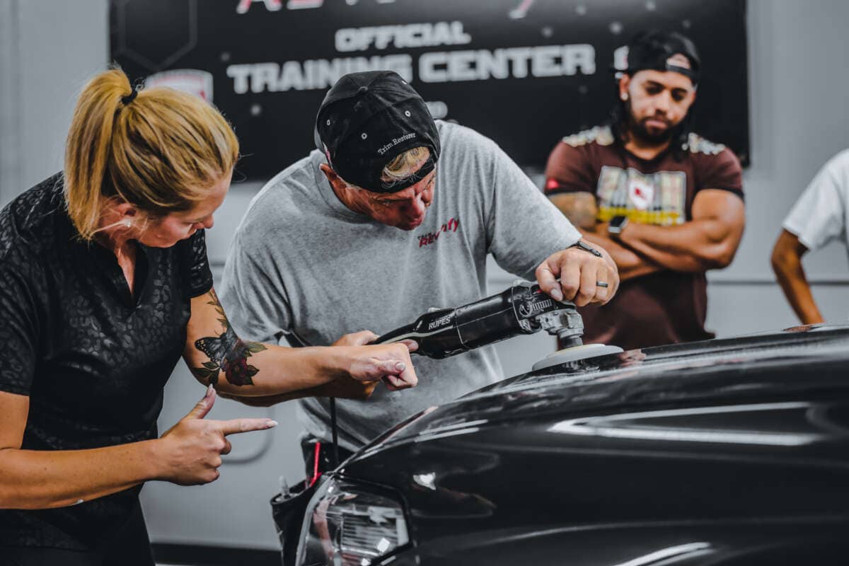 A couple performing total reconditioning on a car in a garage while learning auto detailing training.