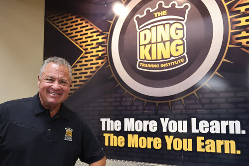 Todd Sudeck, the CEO and Founder of The Ding King Training Institute standing next to a Ding King sign that says "The More Your Learn. The More Your Earn."