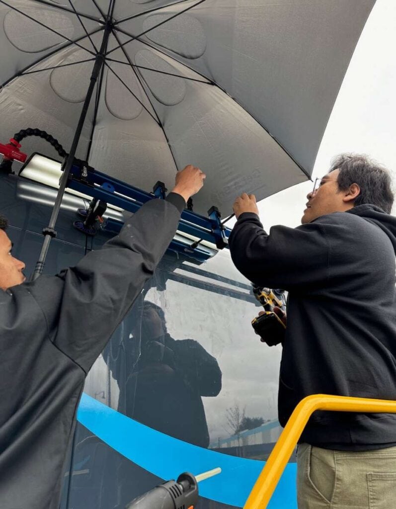 Two individuals installing an umbrella onto a vehicle on an overcast day, seizing an automotive business opportunity.