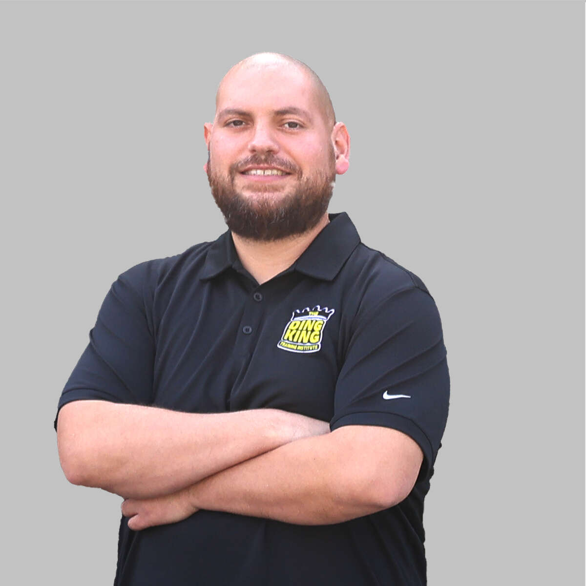 A man with a beard smiling, wearing a black polo shirt with a "Burger King" team logo, standing with his arms crossed against a gray background.