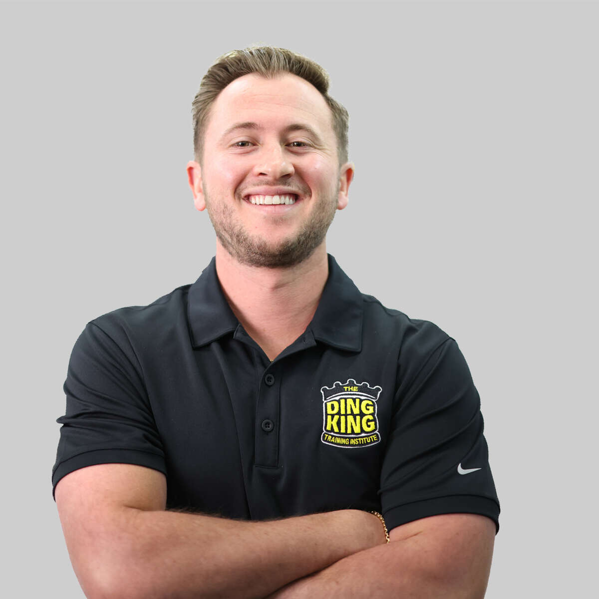 A smiling man in a black team polo shirt with a "ding king" logo, arms crossed, standing against a gray background.