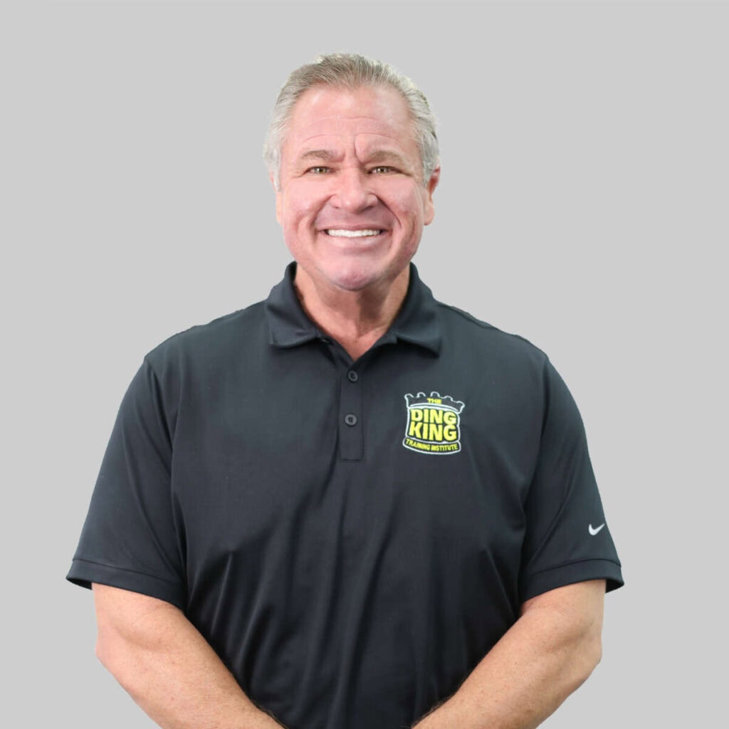 Smiling middle aged man in a black polo shirt with a "ring king" logo, standing against a gray background, ready to meet his team.