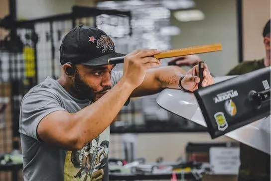 A person wearing a cap measures a surface with a ruler in a workshop, focusing intently on the task at hand as part of an Advanced PDR Training session.