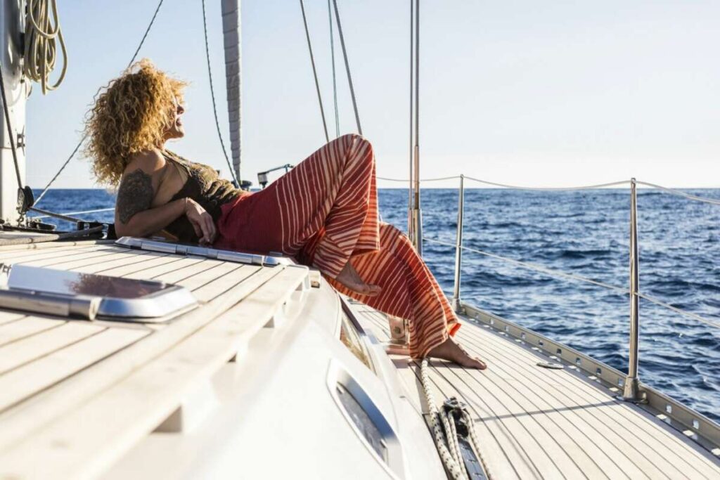 A person reclines on the deck of a sailboat, gazing out at the ocean, with blue water and a clear sky in the background, contemplating their recent Paint Protection Film Training.