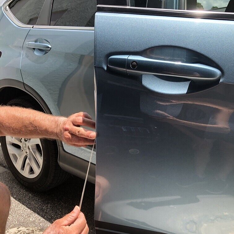 A person is applying a protective strip on the edge of a gray car door near the handle, showcasing skills possibly gained from Paint Protection Film Training. Another car is parked next to it.