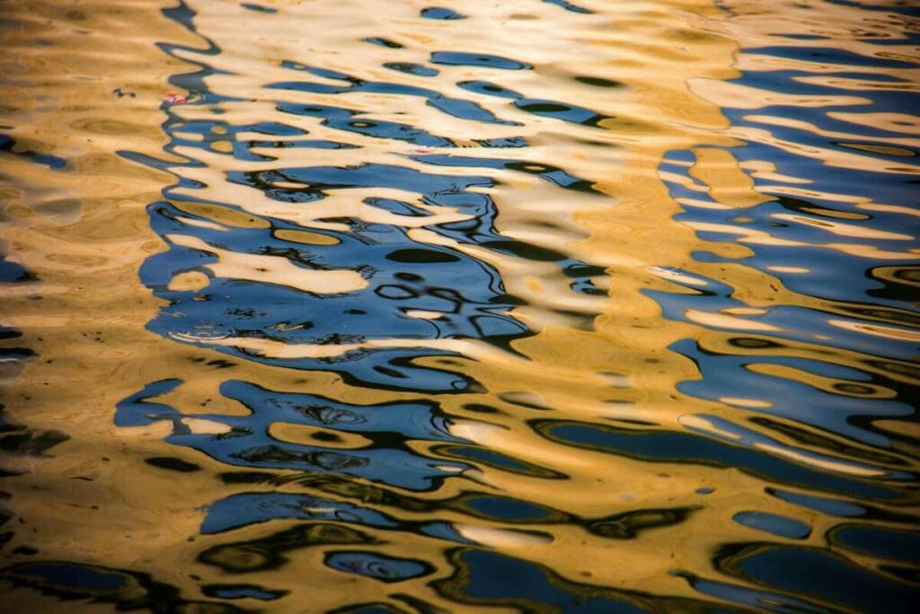 Ripples on water create a mesmerizing pattern of reflections in shades of blue and gold, reminiscent of the intricate detail one might achieve through Paint Protection Film Training.