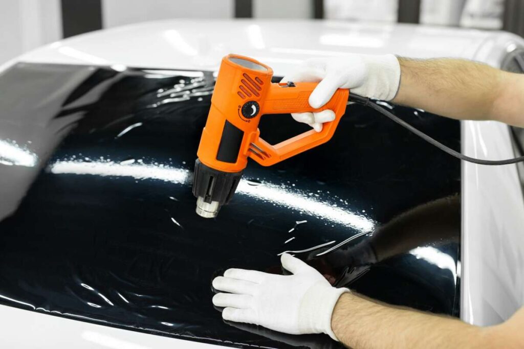 Car tinting - a worker applying tinting foil to the car window with a hair dryer.