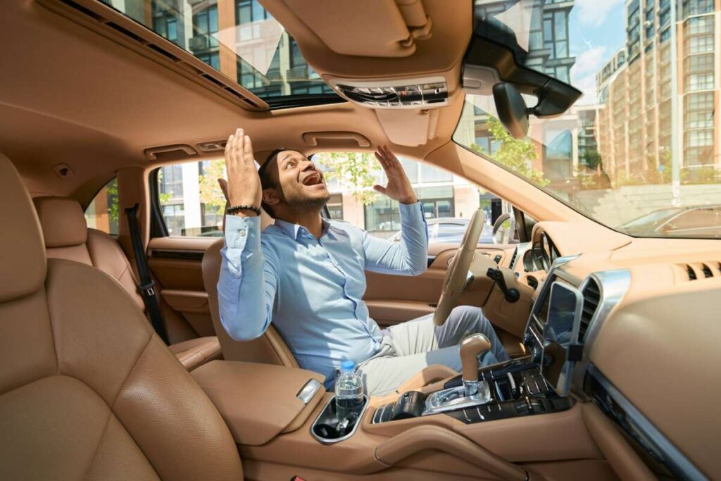 Delighted car driver looking up through open sunroof