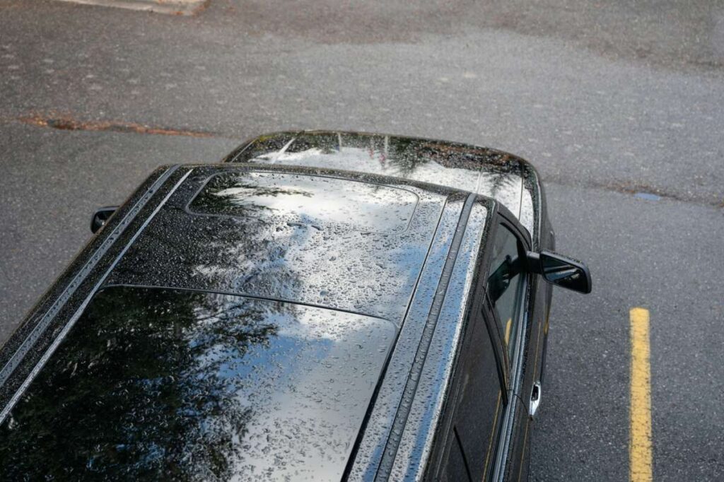 Raindrops falling on the roof of black SUV car on parking