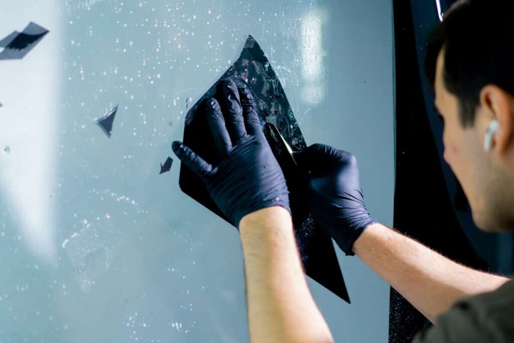 the mechanic cuts off excess pieces of tinting protective film with a clerical knife detailing