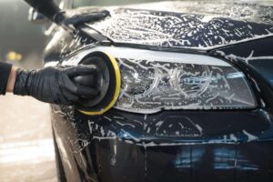 Man cleans car lamp with circle sponge. Preparing auto for polishing. Detailed car wash